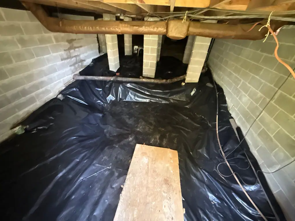 Fresh black vapor barrier laid in a crawlspace between the block piers