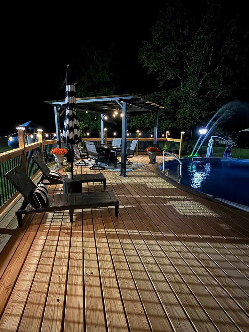 Pool deck at night with string lights, loungers and a pergola