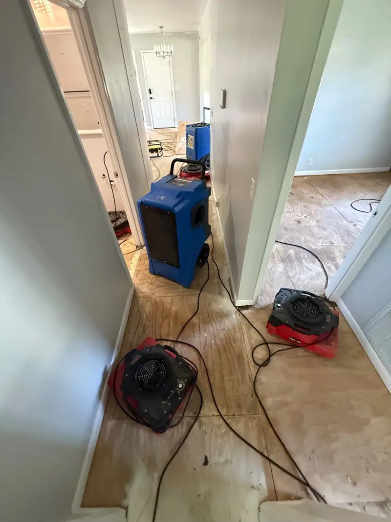 Dehumidifier and air movers lined up down a hallway on bare subfloor