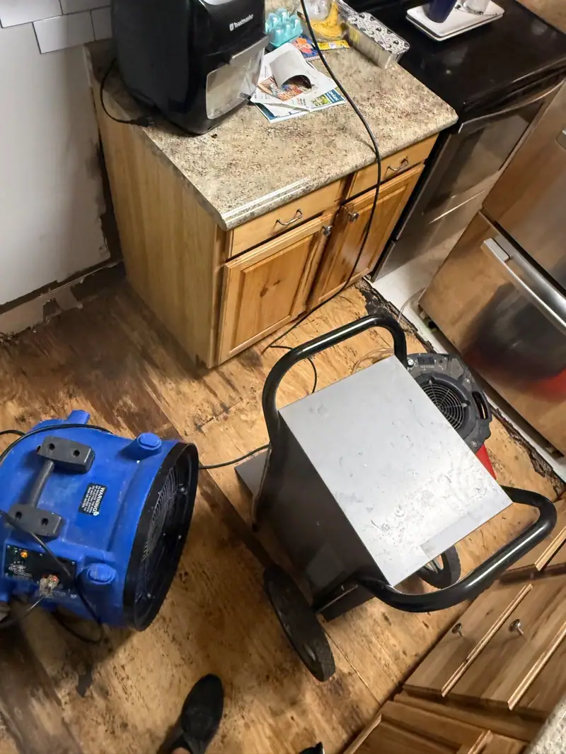 Air mover and dehumidifier drying a kitchen floor beside the cabinets