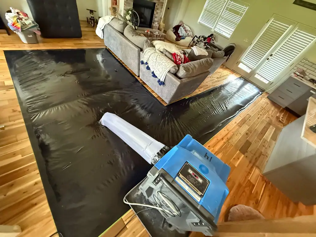 Black floor-drying mats pulling water out of a hardwood living room floor